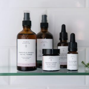 PURA NORDICA luonnonkosmetiikkaa ruskeissa pulloissa lasihyllyllä, valkoista kaakeliseinää vasten