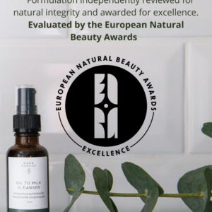 PURA NORDICA Emulgoituva puhdistusöljy -pullo lasihyllyllä ja vieressä ENBA logo